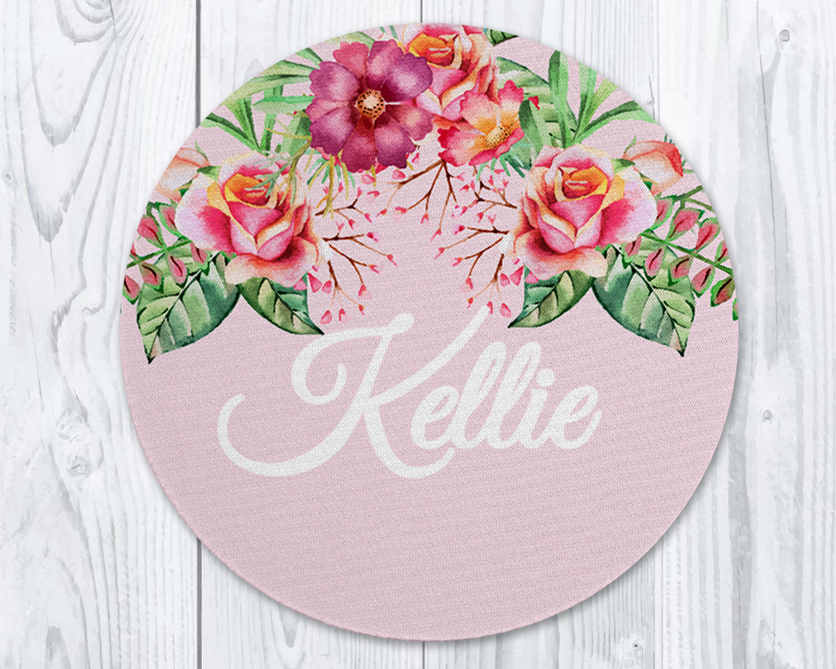 Round pink placemat with floral design and &#39;Kellie&#39; text on a white wooden surface