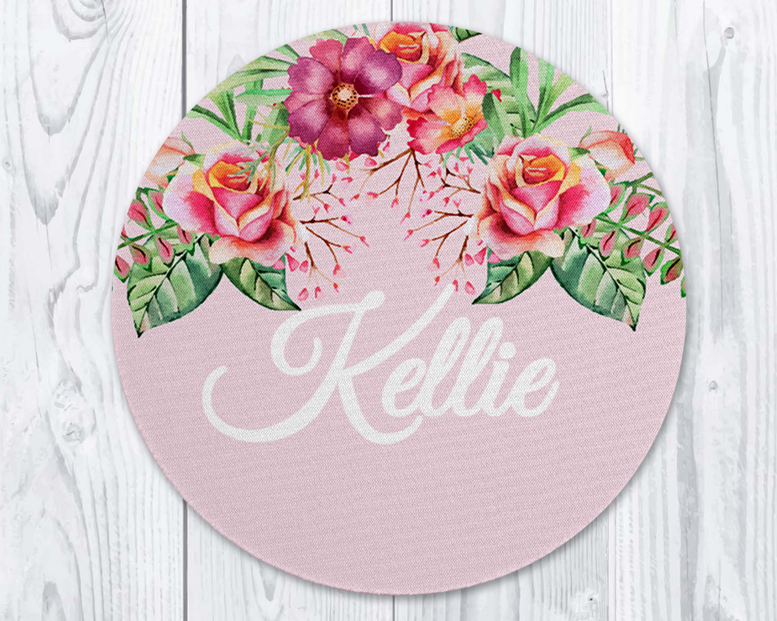 Round pink placemat with floral design and 'Kellie' text on a white wooden surface